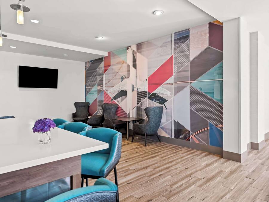 Un hall d’hôtel moderne avec un comptoir d’accueil blanc, des chaises turquoise et une fresque murale géométrique aux couleurs vives.