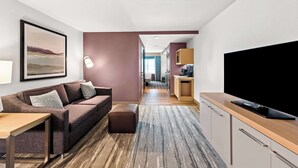 Una habitación de hotel moderna con sofá, televisor, mesita de madera y un cuadro grande en la pared.