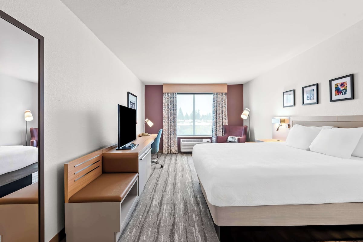 A hotel room with a large bed, a desk with a chair, a television, and a window with curtains.