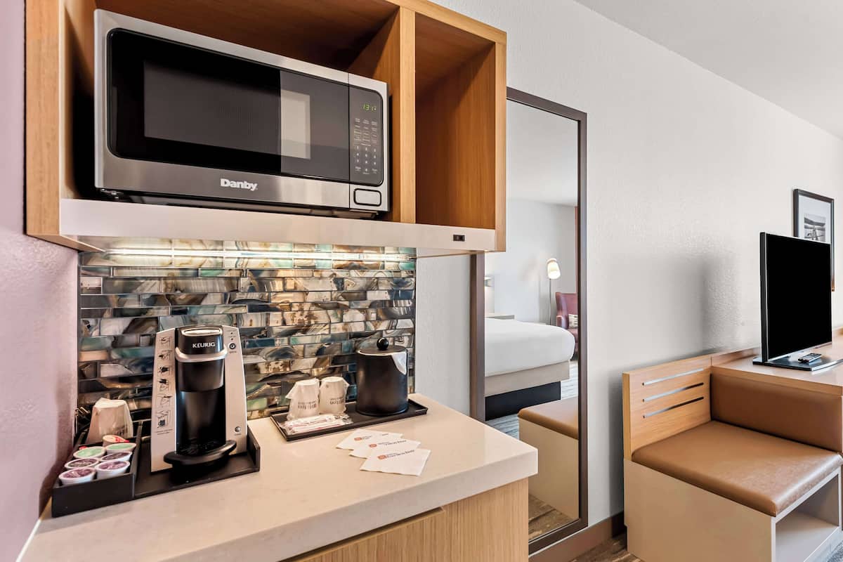 A compact hotel room with a kitchenette, including a microwave, coffee machine, and a small refrigerator.