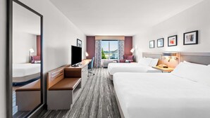 Habitación de hotel con dos camas, un escritorio, un televisor y ventana con vistas.