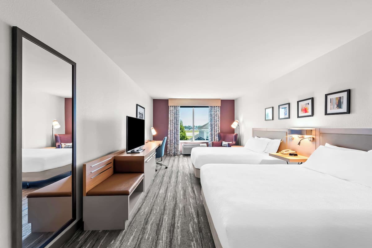 A hotel room with two beds, a desk, a TV, and a window with a view.