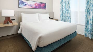 A hotel room with a large bed, a bedside table with a lamp, a painting on the wall, and a window with curtains.
