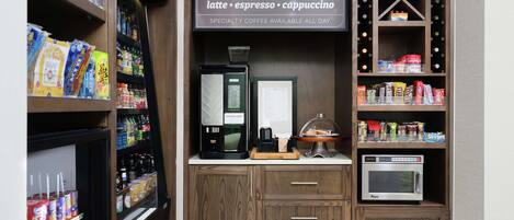 A coffee station with a coffee machine, a menu board, and shelves stocked with snacks and beverages.