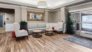 A lobby with a sofa, two armchairs, a round table, a mirror, and a large window. - Hilton Garden Inn Ithaca (Ithaca)