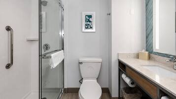 A modern bathroom with a glass shower enclosure, a toilet, a sink with a marble countertop, and a framed picture on the wall.