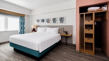 A hotel room with a bed, a nightstand, a lamp, a wall-mounted phone, a window with curtains, and a wooden wardrobe.