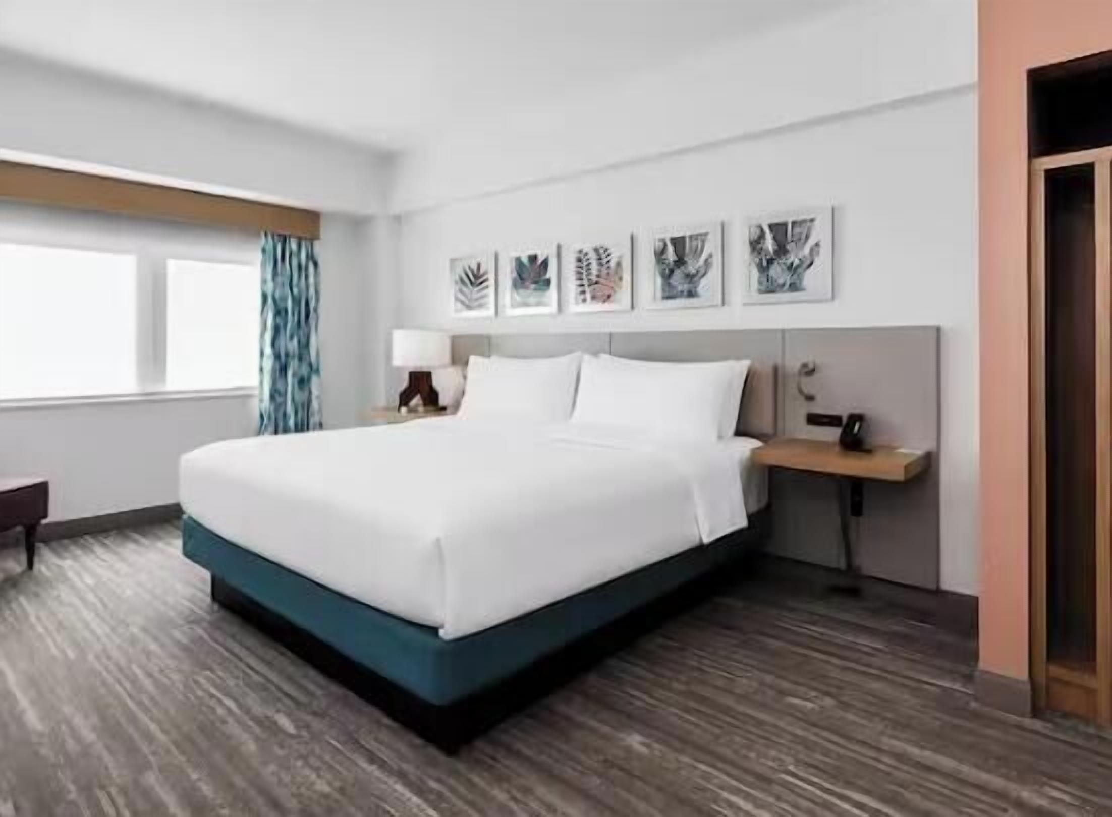 Een hotelkamer met een groot bed, een bureau, een stoel, een raam met gordijnen en kunst aan de muur.