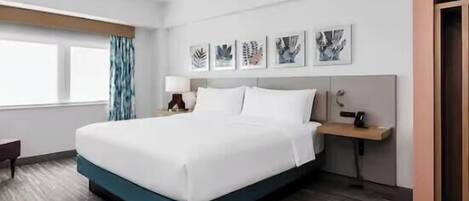 Een hotelkamer met een groot bed, een bureau, een stoel, een raam met gordijnen en kunst aan de muur.