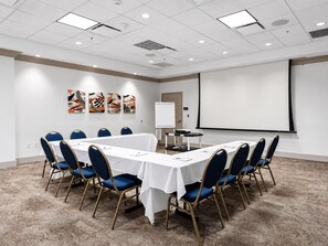 Un salón de conferencias con una larga mesa, sillas azules, una pizarra y una pantalla de proyector.