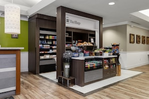 A store interior with shelves stocked with various products, a sign reading 'The Shop,' and a patterned light fixture. - Hilton Garden Inn Ithaca (Ithaca)