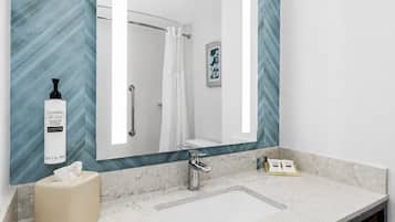 Une salle de bain avec un grand miroir, un lavabo, un distributeur de serviettes et un rideau de douche.