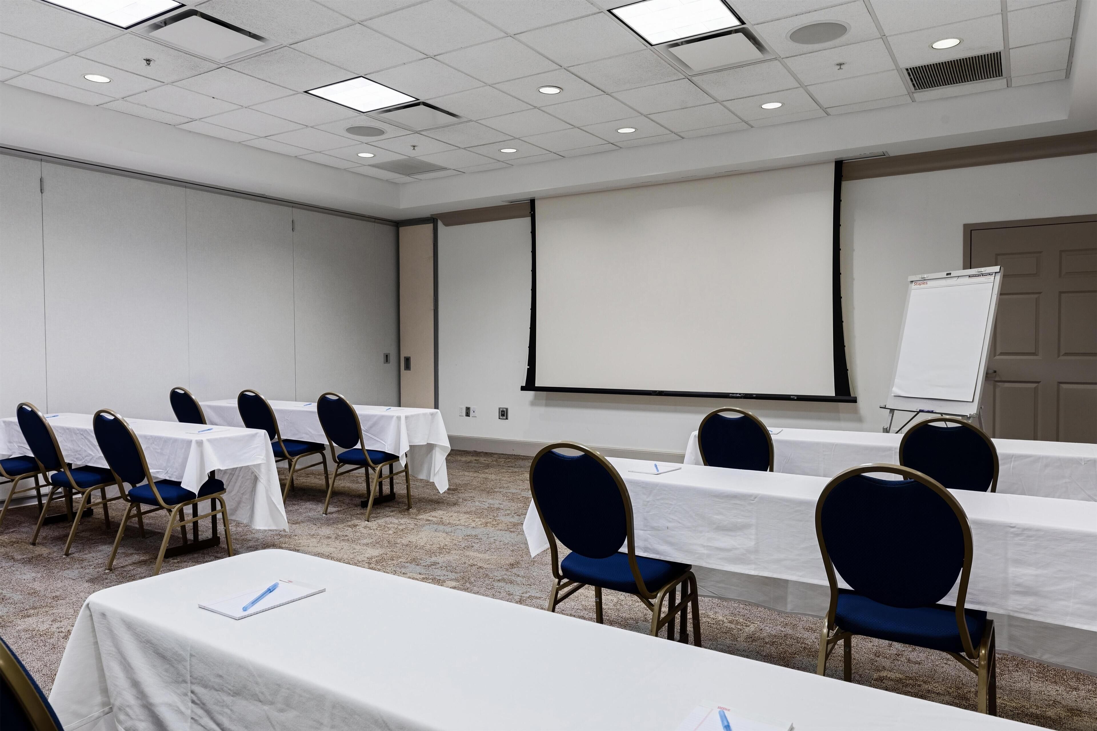 A conference room with tables, chairs, a projector screen, and a whiteboard.