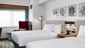 A hotel room with two beds, a red armchair, a floor lamp, and artwork on the wall.