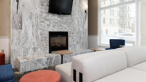 A modern living room with a fireplace, a flat-screen TV mounted on a marble wall, and seating arrangements. - Hilton Garden Inn Ithaca (Ithaca)