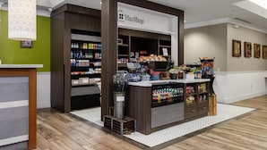 A store interior with shelves stocked with various products, a sign reading 'The Shop,' and a patterned light fixture. - Hilton Garden Inn Ithaca (Ithaca)