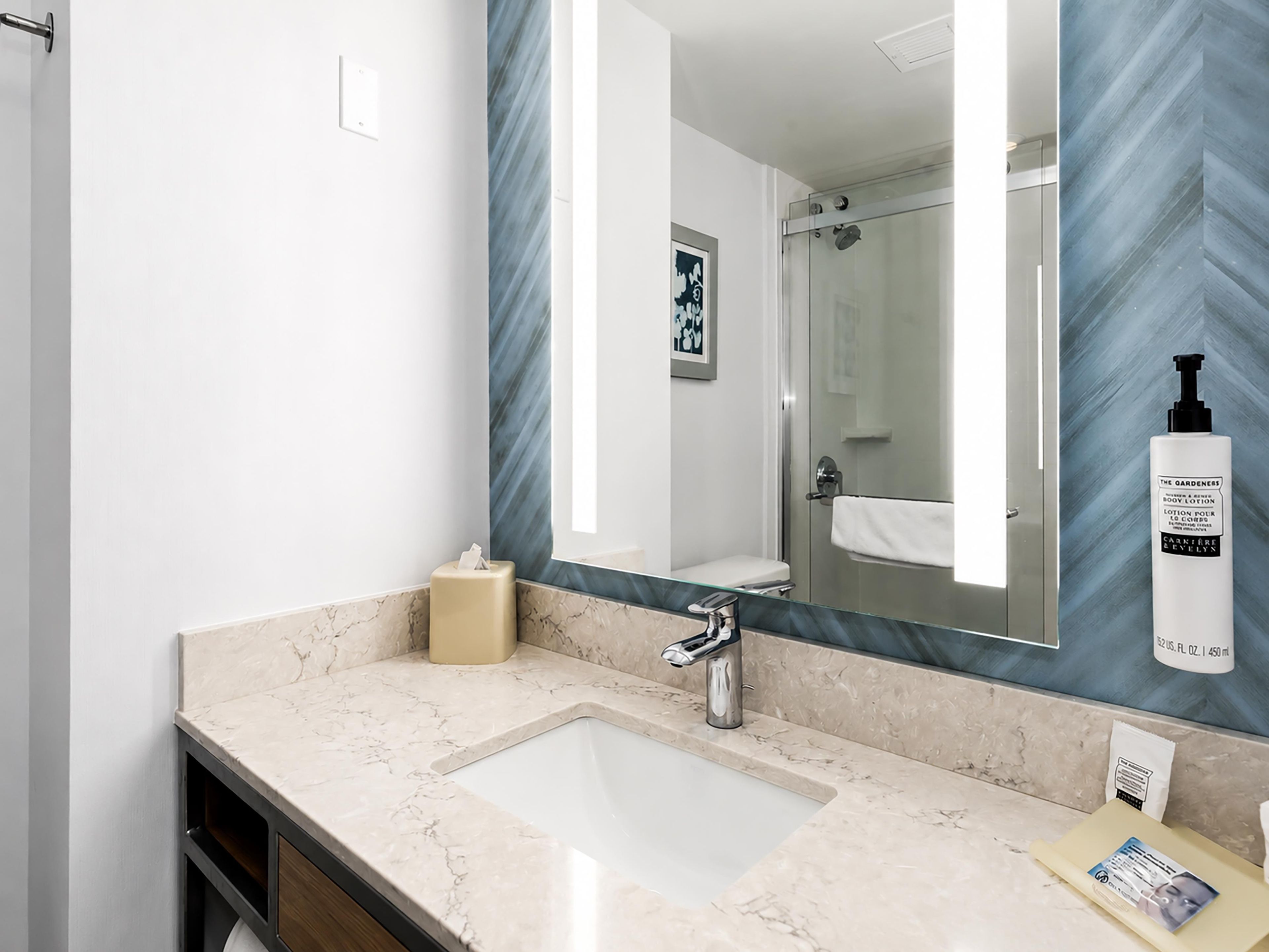 A bathroom with a marble sink, a mirror, a towel rack, and a shower.