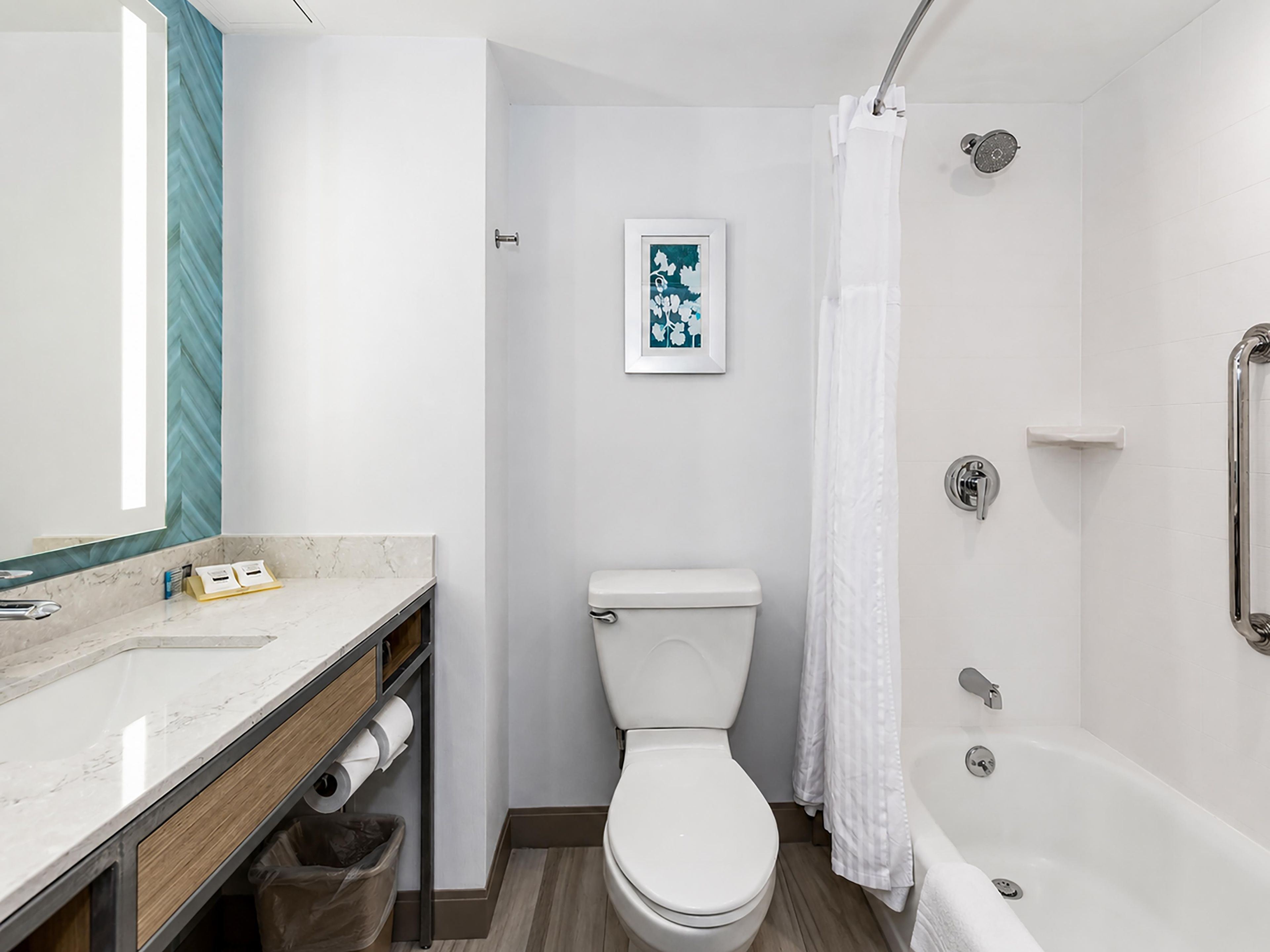 A bathroom with a toilet, shower, and a sink with a mirror.