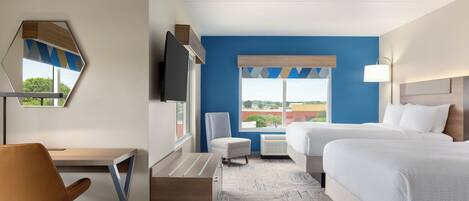 Habitación de hotel con cama, escritorio, silla, televisión y ventana con vistas a edificios.