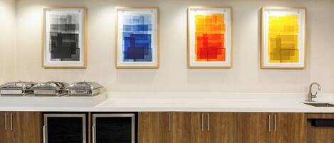Una cocina moderna con encimera blanca, armarios de madera y cuatro cuadros abstractos enmarcados.