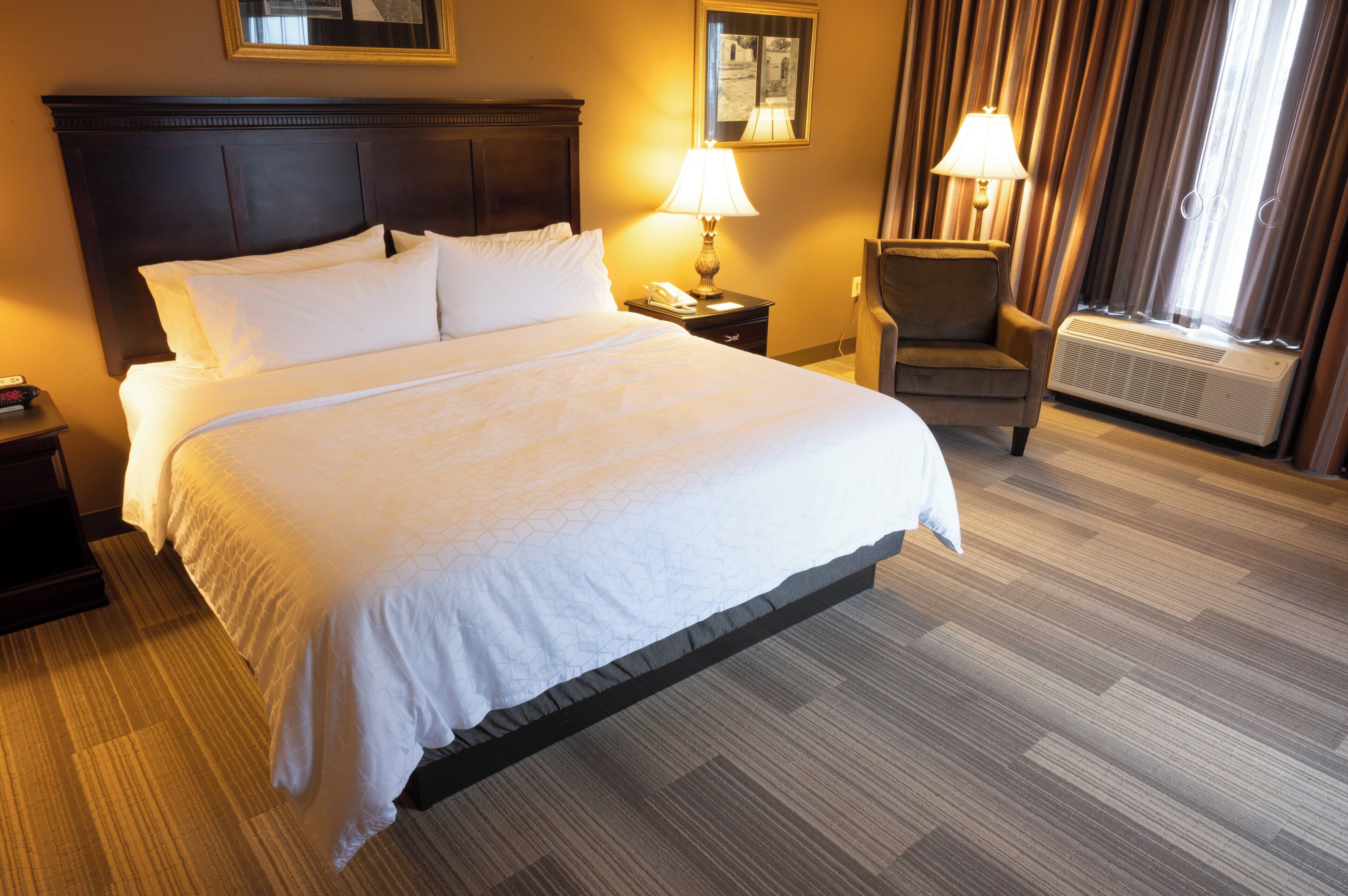 A hotel room with a large bed, two bedside tables, a chair, a lamp, and a window with curtains.