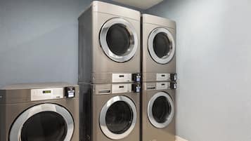 Cuatro lavadoras de carga frontal apiladas en una habitación con paredes azul claro y suelo de baldosas.