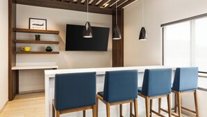 Una cocina moderna con encimera blanca, taburetes azules, vigas de madera e iluminación colgante.