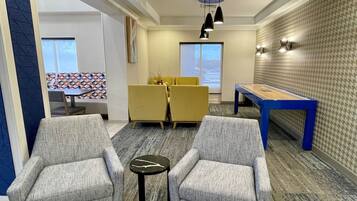 A modern lounge area with two armchairs, a small round table, a blue pool table, and a dining set.