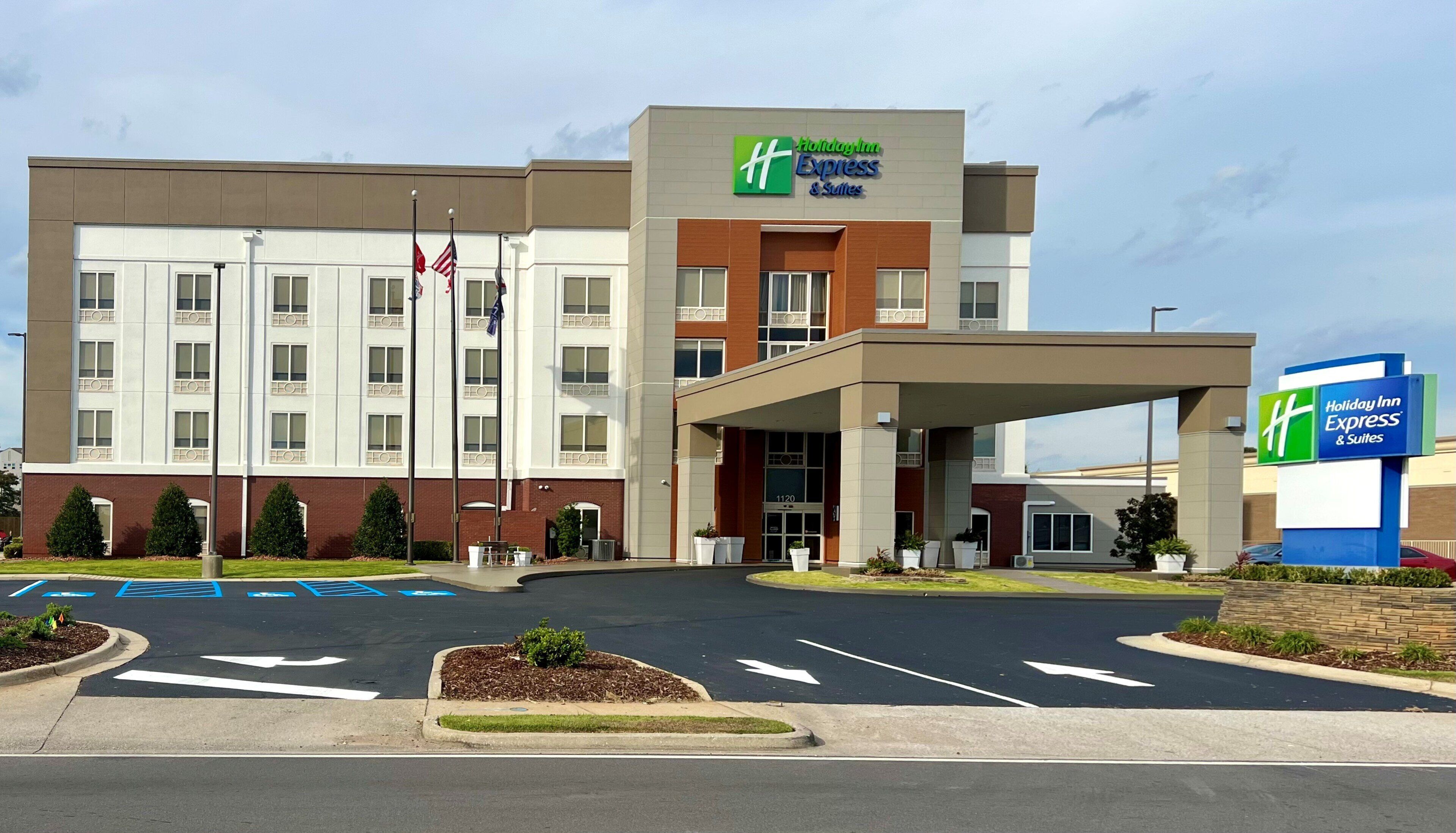 A Holiday Inn Express & Suites building with a covered entrance, marked parking spaces, and a clear sky.
