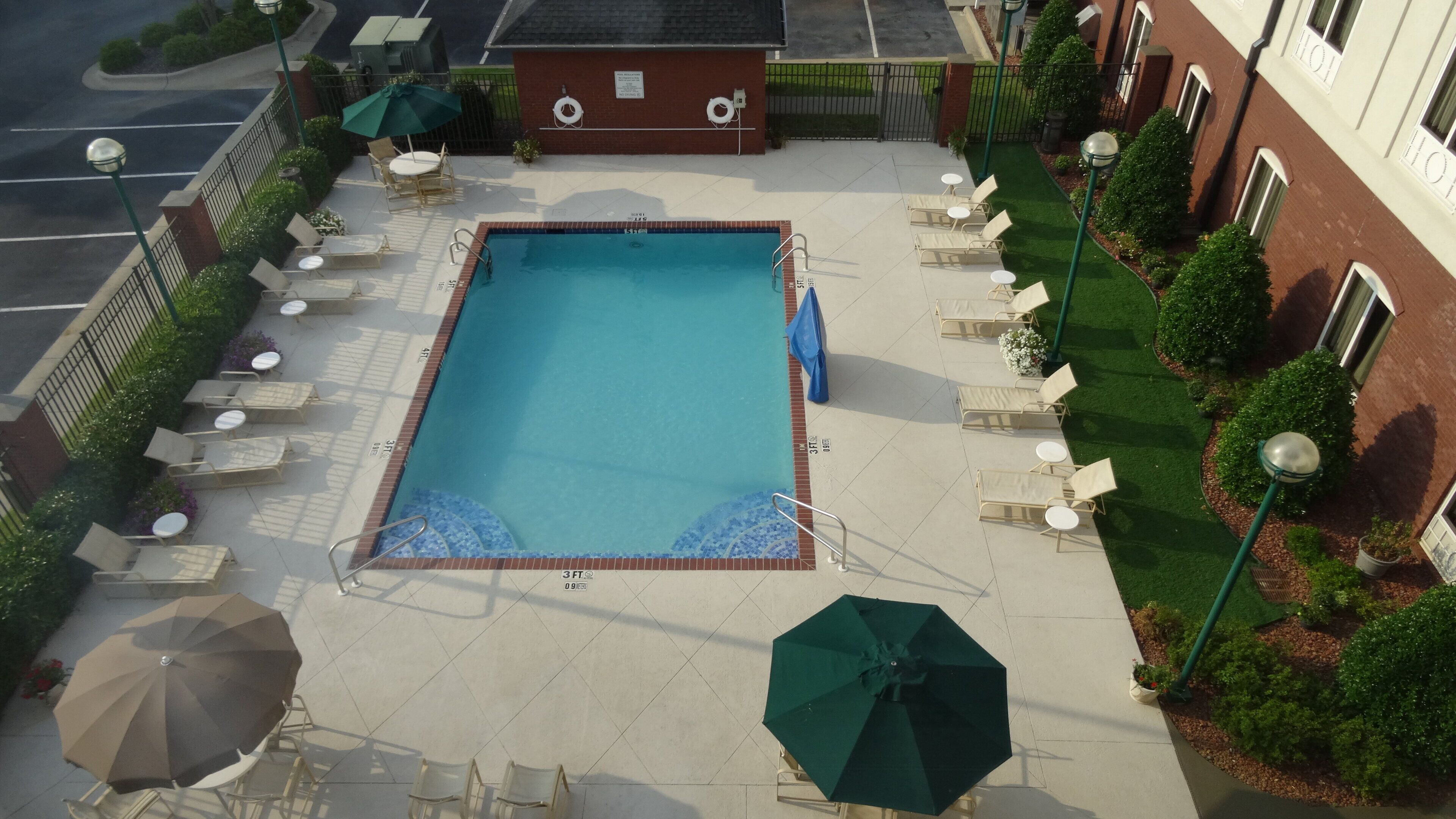 Una piscina sul tetto con poltrone a sdraio e ombrelloni, immersa in un edificio in mattoni e verde circostante.