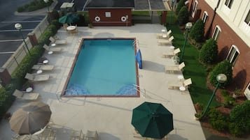 Una piscina sul tetto con poltrone a sdraio e ombrelloni, immersa in un edificio in mattoni e verde circostante.