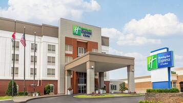 Edificio de Holiday Inn Express & Suites con un acceso cubierto, banderas estadounidenses y un área ajardinada con plantas.