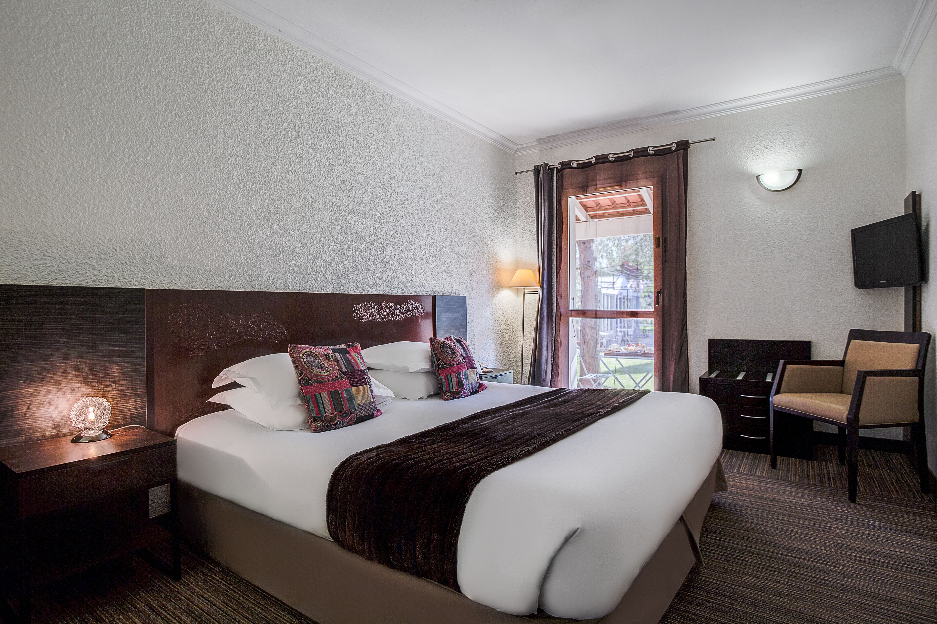 A hotel room with a large bed, a bedside lamp, a TV, and a chair.