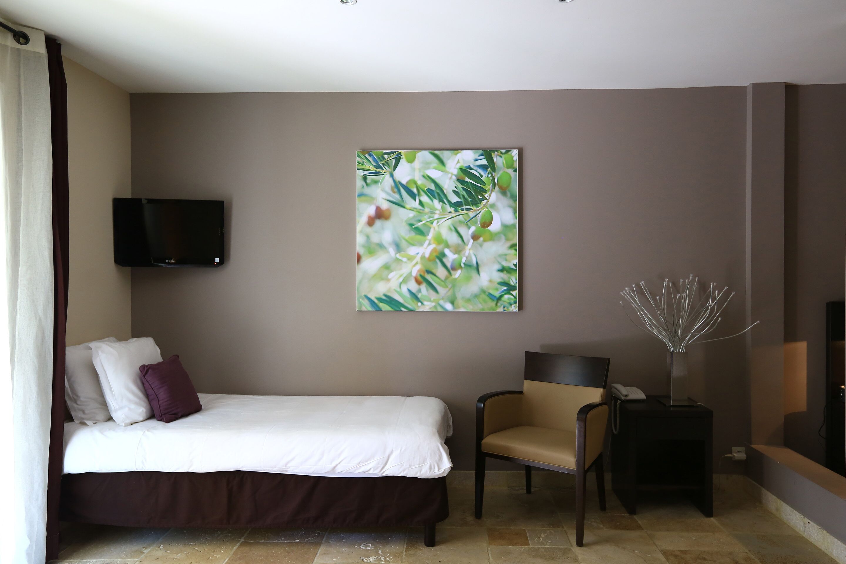 Ein Hotelzimmer mit einem Bett, einem Sessel, einem Flachbildfernseher und einem an der Wand befestigten Kunstwerk.
