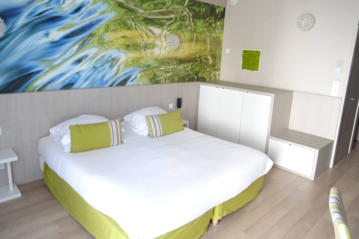 Ein Hotelzimmer mit einem großen Bett, einem Kleiderschrank, einem Nachttisch und einer Wand in Grünton.