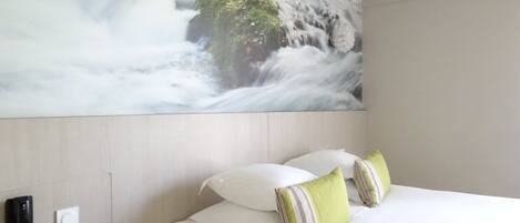 Habitación de hotel con cama, almohadas, mesita de noche, teléfono y un gran mural en la pared con una cascada.