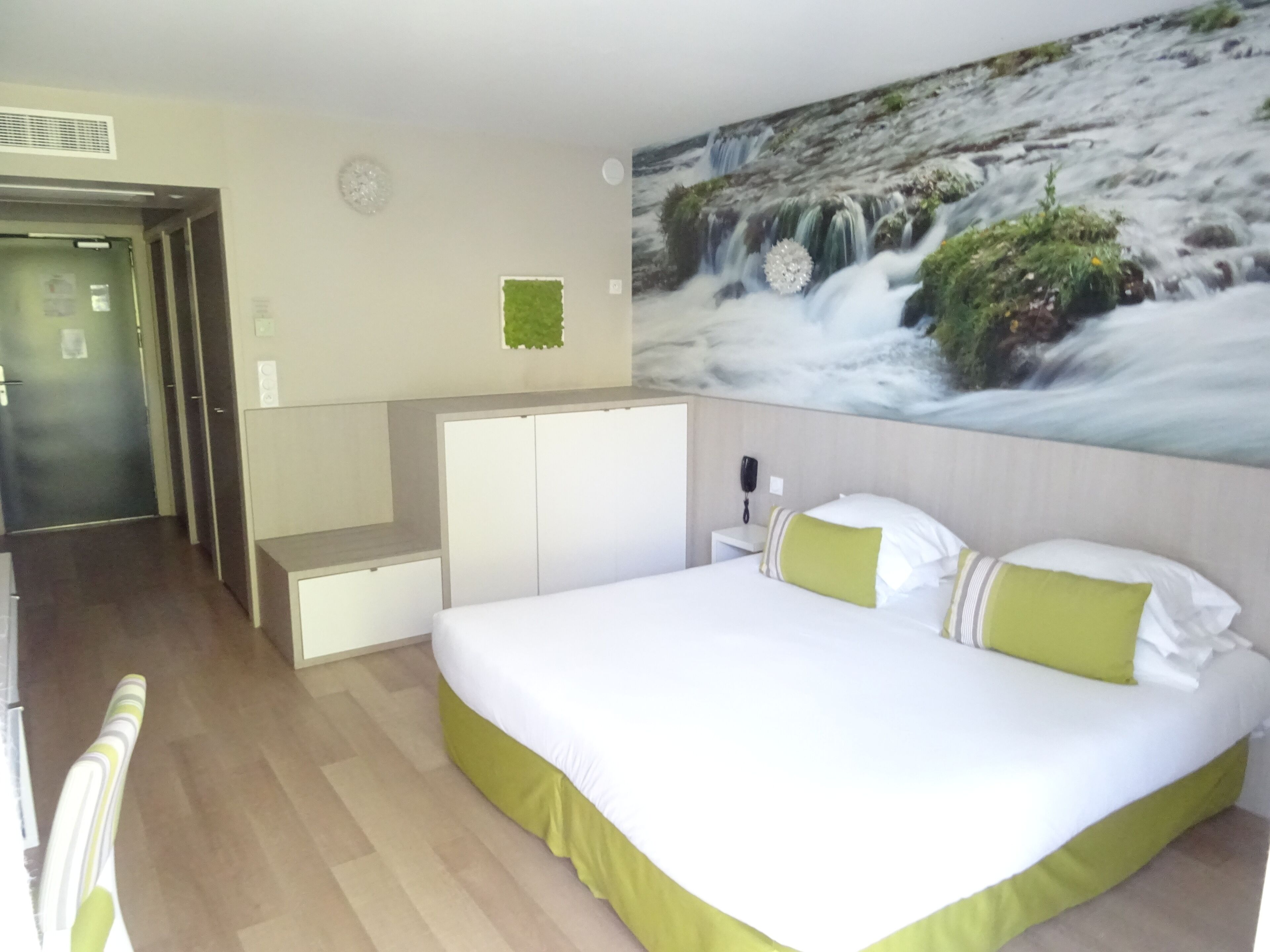 A hotel room with a bed, a desk, a wardrobe, and a wall-mounted phone.
