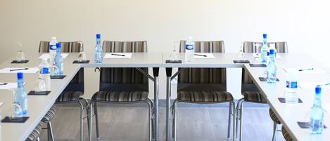 A conference room with a long table, chairs, water bottles, and a glass dispenser.