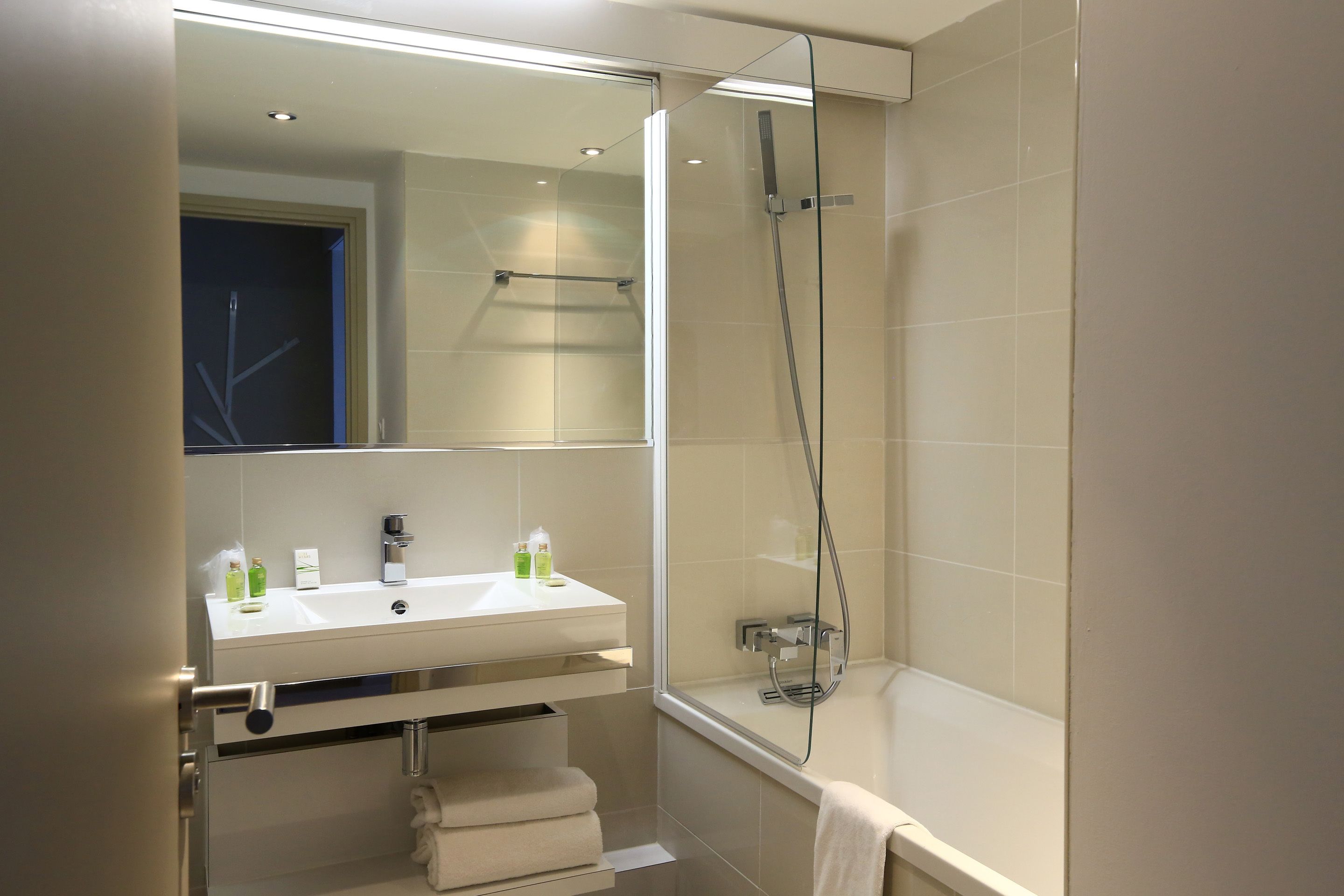A modern bathroom with a glass-enclosed shower, a white sink with two faucets, and a visible towel rack.