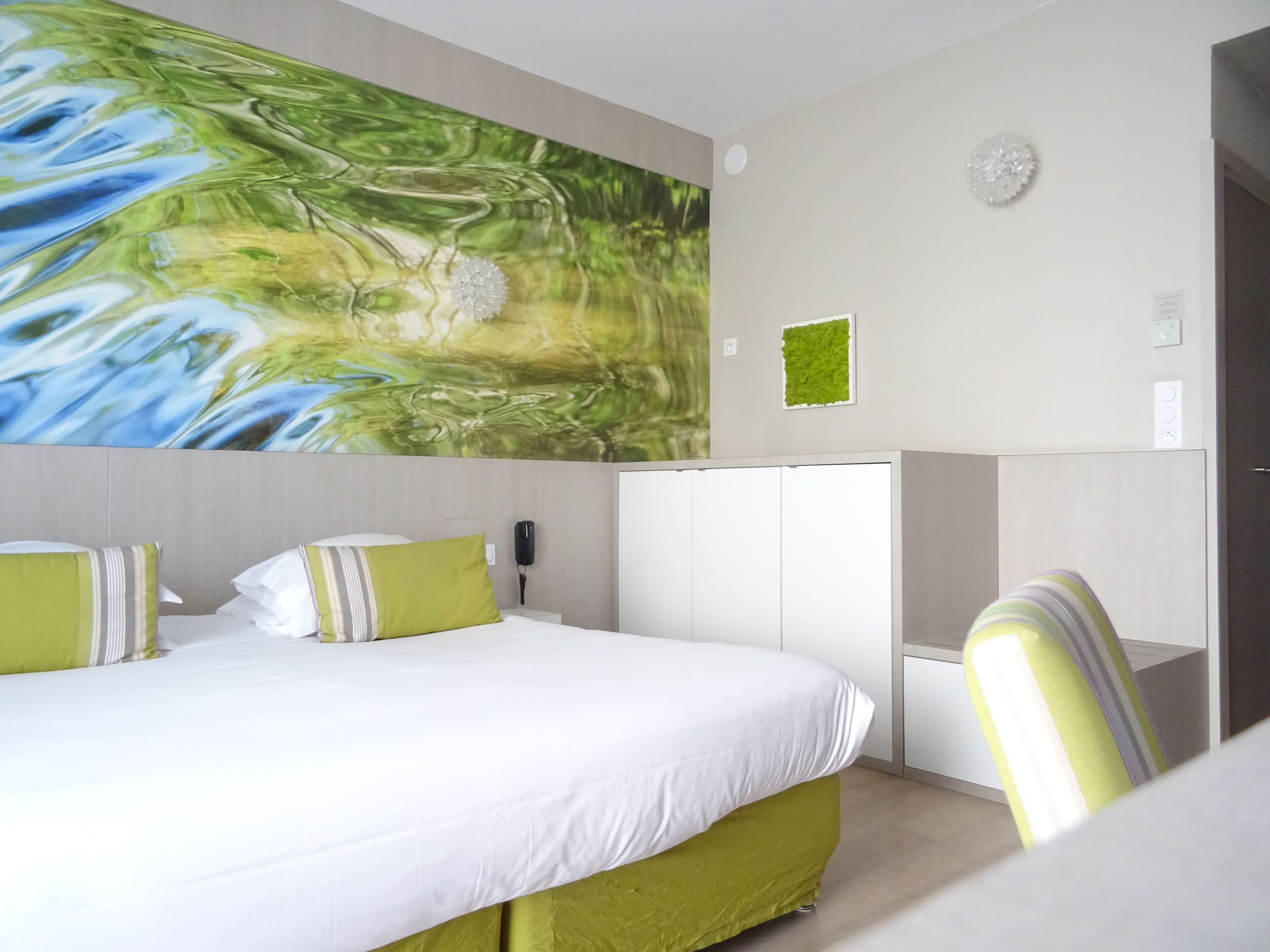 A hotel room with a bed, a green accent wall, a white wardrobe, and a green chair.