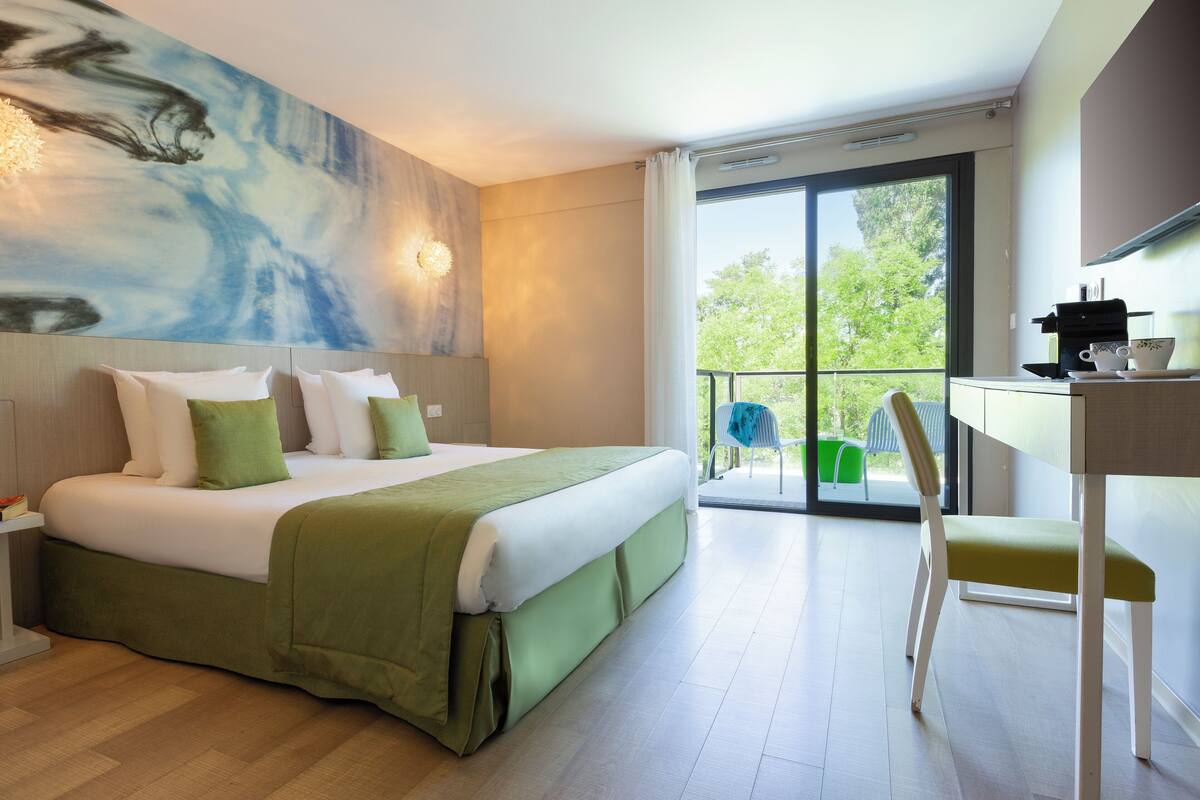 Ein modernes Hotelzimmer mit einem großen Bett, einem Balkon mit Blick und einer kleinen Küchenzeile.
