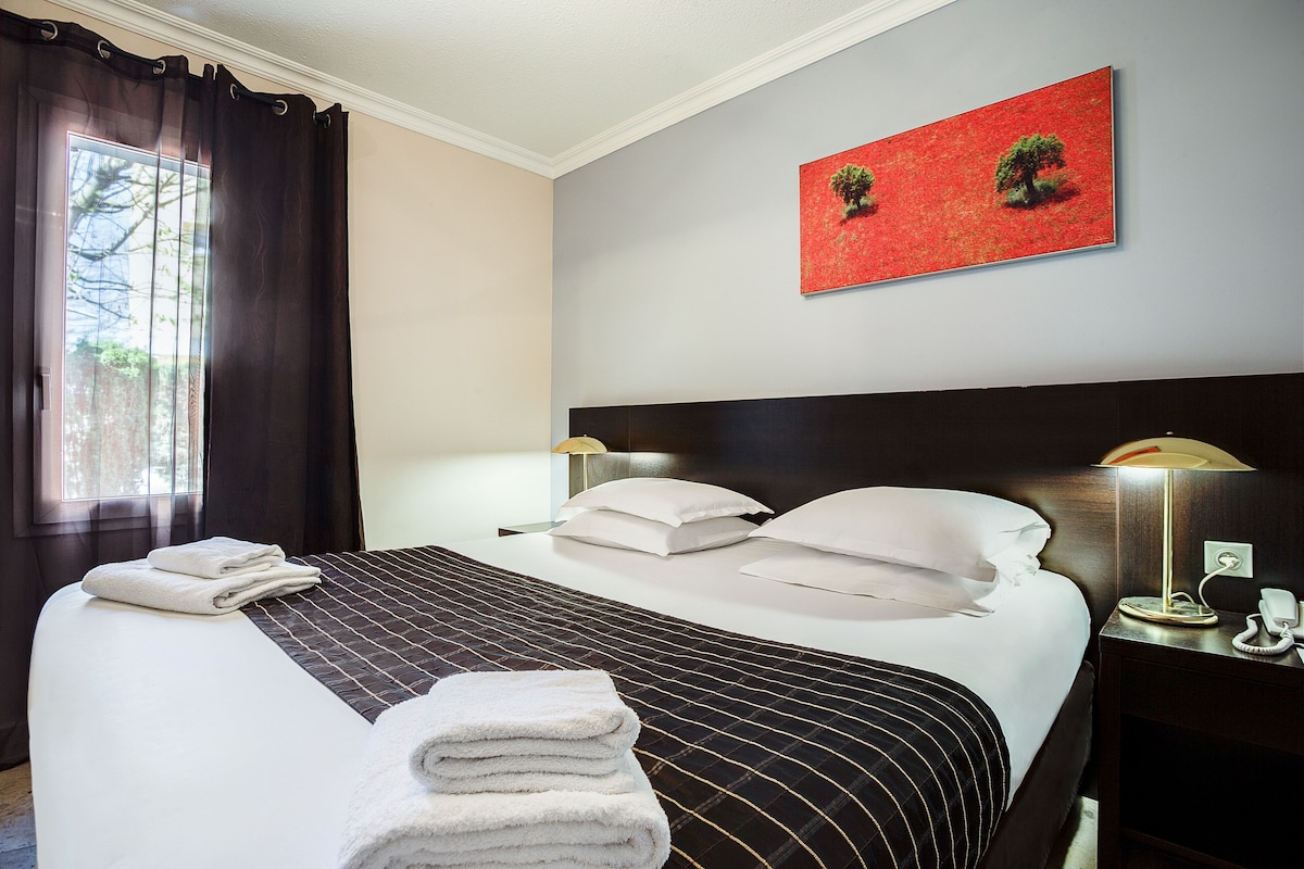 Ein Hotelzimmer mit einem großen Bett, zwei Nachttischlampen, einem Nachttisch mit Telefon und einem roten Kunstwerk an der Wand.