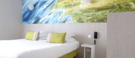 Quarto de hotel moderno com uma cama grande, roupa de cama verde e branca, uma mesa de cabeceira com telefone e um quadro abstrato grande na parede.