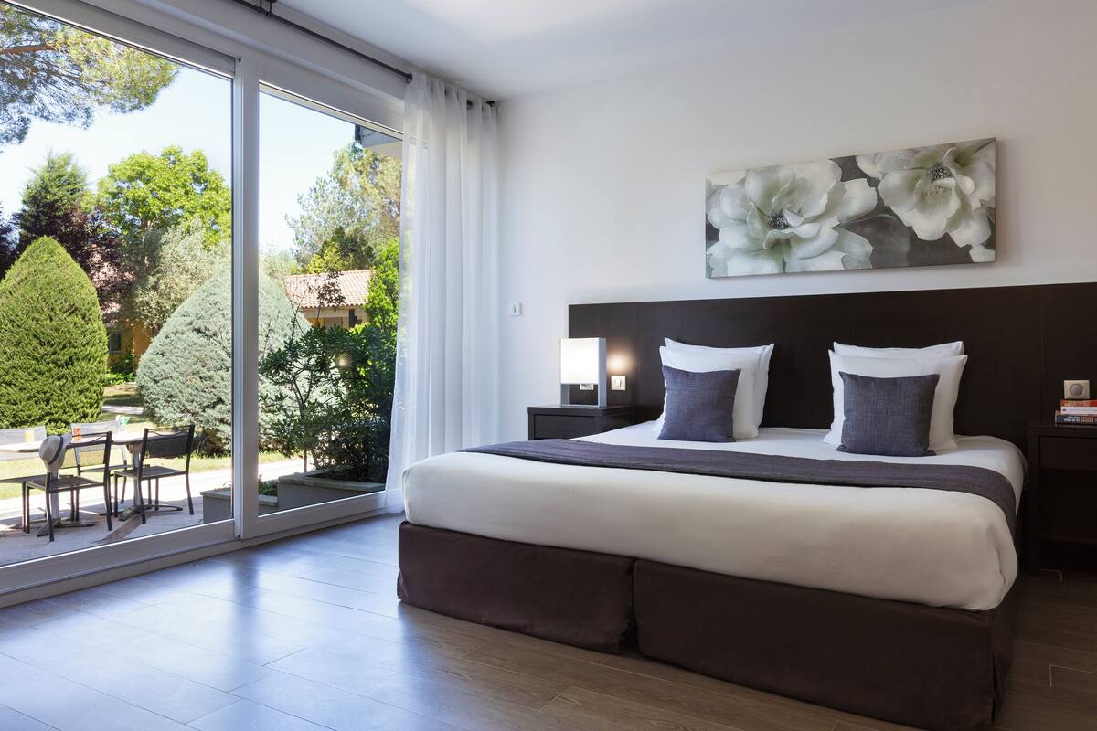 Ein modernes Schlafzimmer mit großem Bett, Blick auf den Garten und einem Essbereich mit Stühlen.