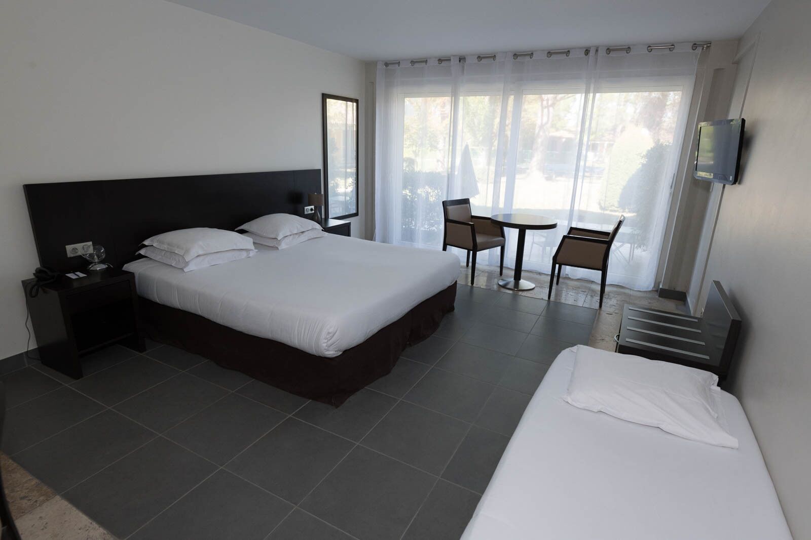 Ein Hotelzimmer mit einem großen Bett, einem kleineren Bett, einem Schreibtisch, einem Sessel und einem Fernseher.