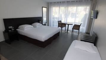 Ein Hotelzimmer mit einem großen Bett, einem kleineren Bett, einem Schreibtisch, einem Sessel und einem Fernseher.