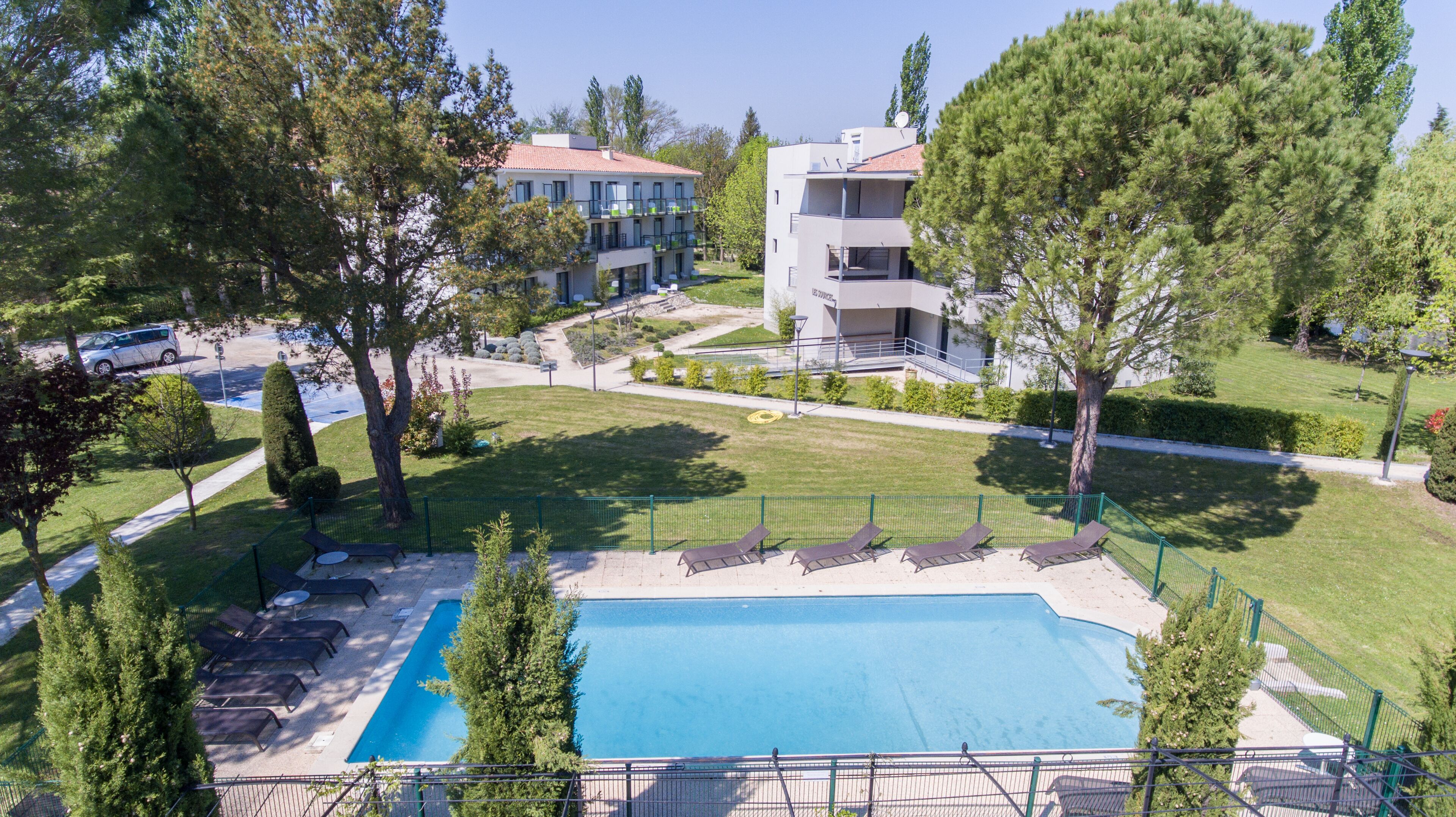 A pool area with lounge chairs, surrounded by a fence, and adjacent to a building with multiple balconies.