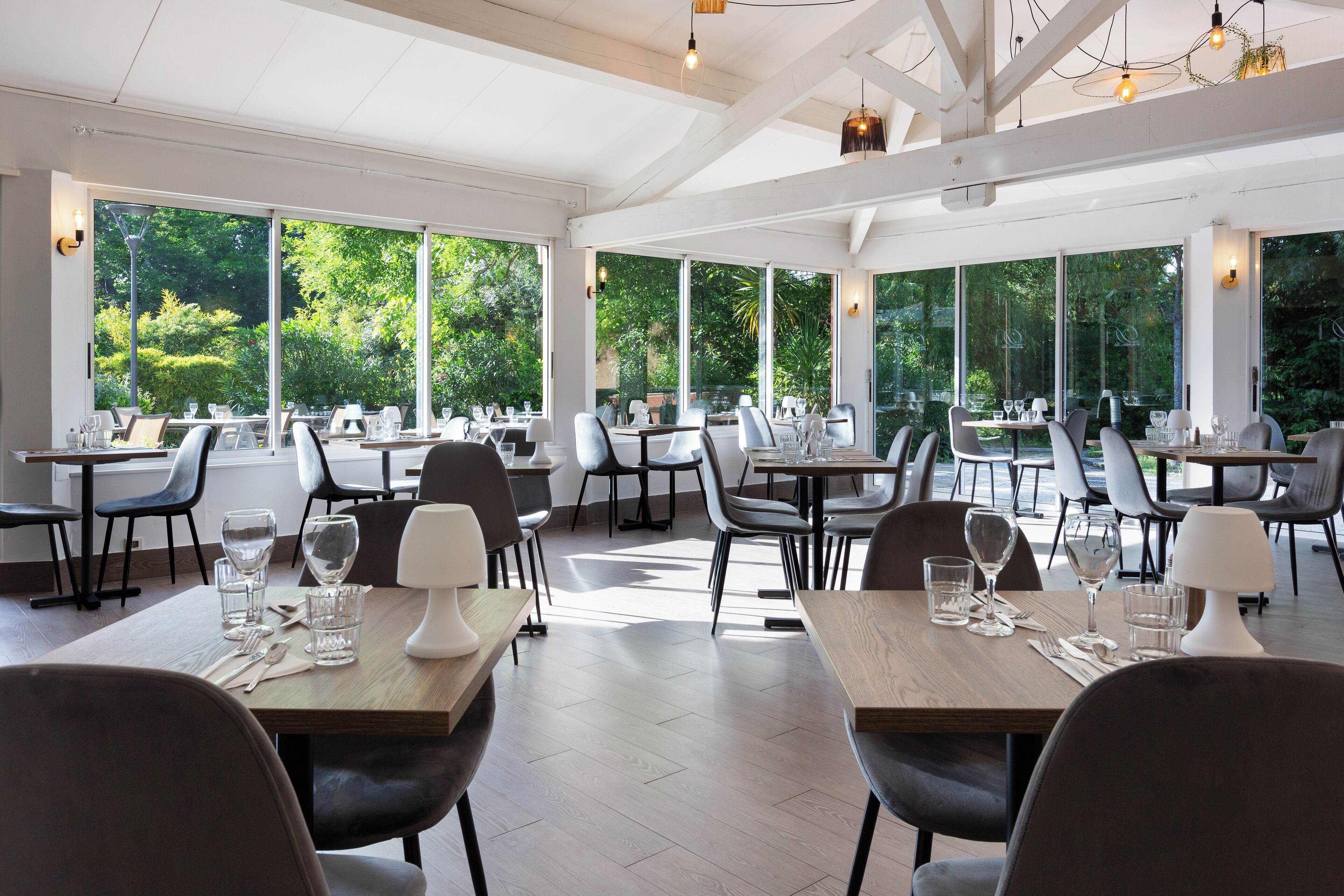 Un ristorante moderno con ampie finestre, tavoli di legno e sedie nere.