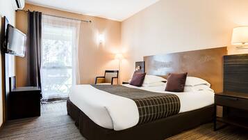 A hotel room with a large bed, a flat-screen TV, a desk, and a chair.