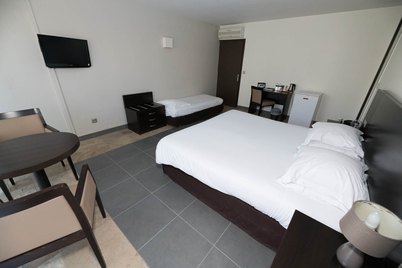Una camera d'hotel con un letto grande, una scrivania, una sedia, un tavolino, una TV fissata al muro e un armadio.